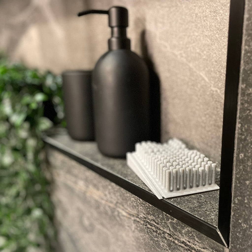 Bathroom shelf with black soap dispenser, cups, and a plant on a stone surface.